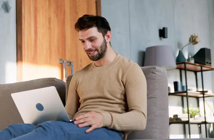 Koltuğa yaslanmış bilgisayar ile çalışan bir adam