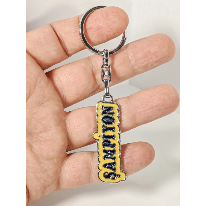 Sarı Üzerine Lacivert  “Şampiyon” Yazılı Metal Anahtarlık – Başarının ve Özgüvenin Simgesi