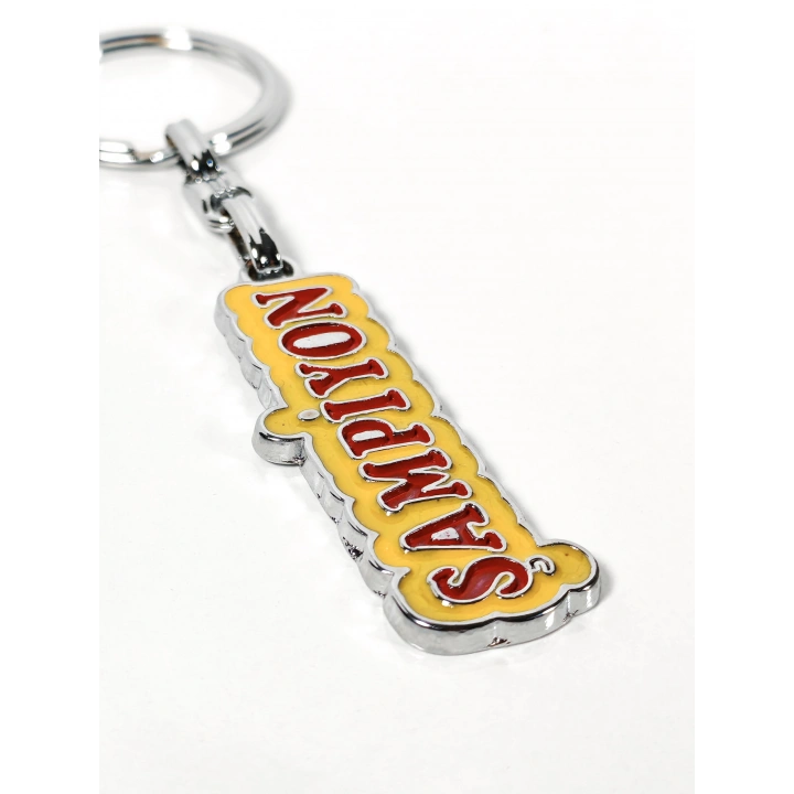 Şampiyon Yazılı Sarı Kırmızı Metal Anahtarlık – Enerjik Tasarım ve Güçlü Duruşun Eğlenceli İfadesi
