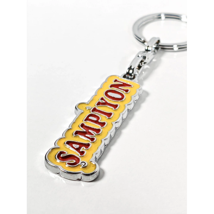 Şampiyon Yazılı Sarı Kırmızı Metal Anahtarlık – Enerjik Tasarım ve Güçlü Duruşun Eğlenceli İfadesi