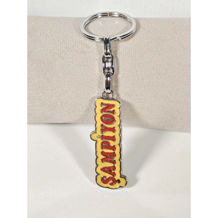 Şampiyon Yazılı Sarı Kırmızı Metal Anahtarlık – Enerjik Tasarım ve Güçlü Duruşun Eğlenceli İfadesi