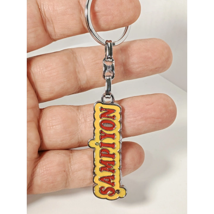 Şampiyon Yazılı Sarı Kırmızı Metal Anahtarlık – Enerjik Tasarım ve Güçlü Duruşun Eğlenceli İfadesi